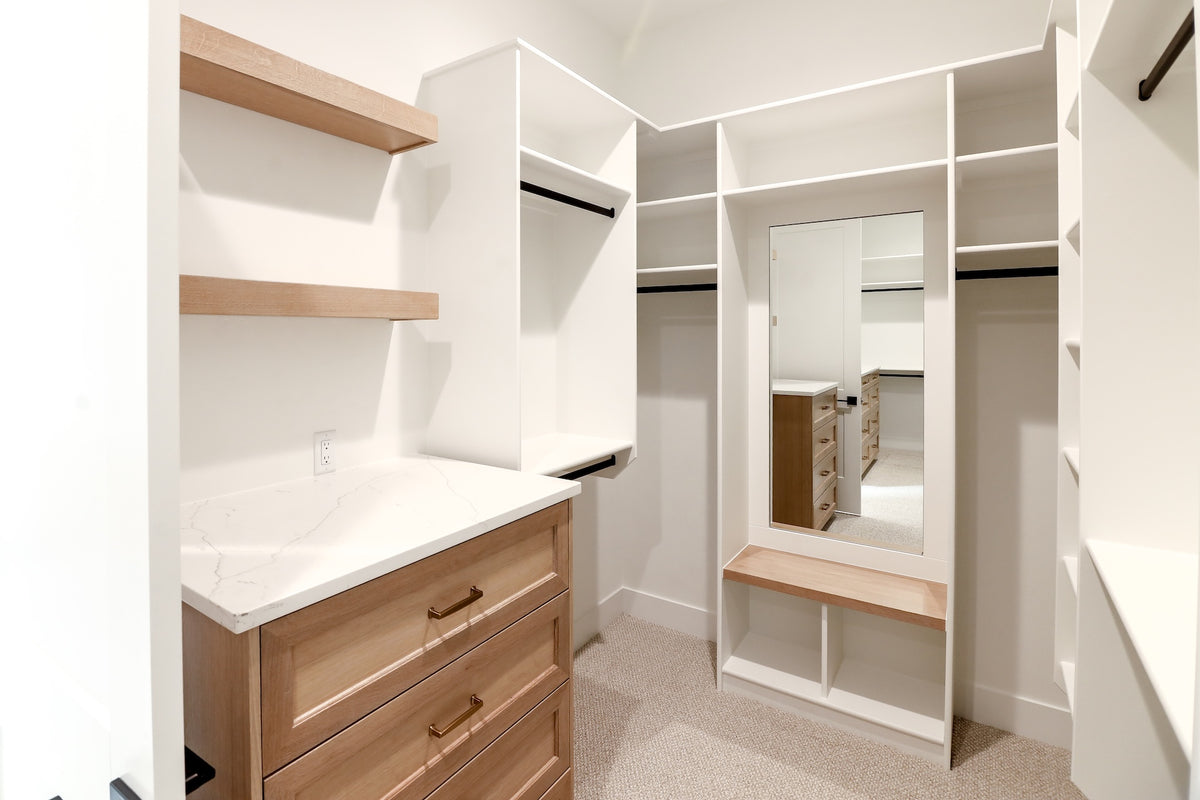 Modern walk-in closet with wooden shelves and drawers, white walls, and a mirror.