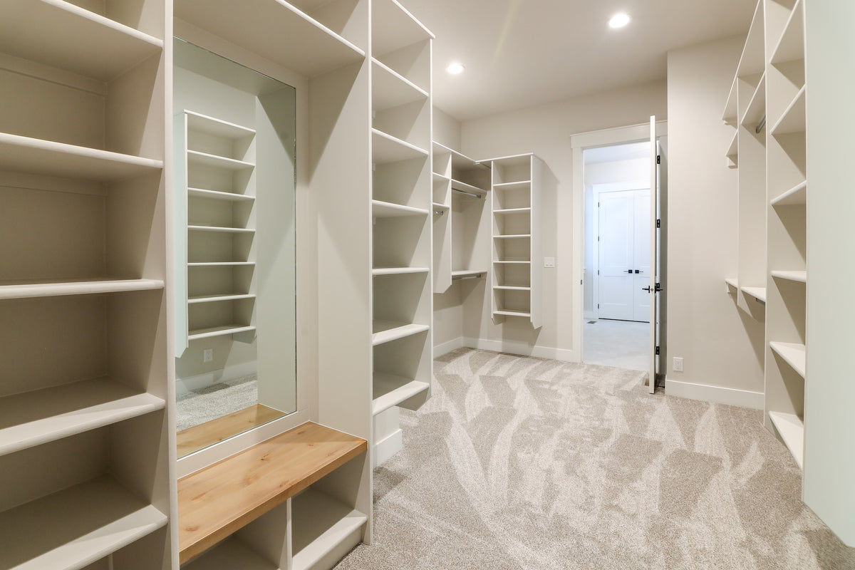 Walk-in closet with white shelves and a wooden bench in a well-lit room.