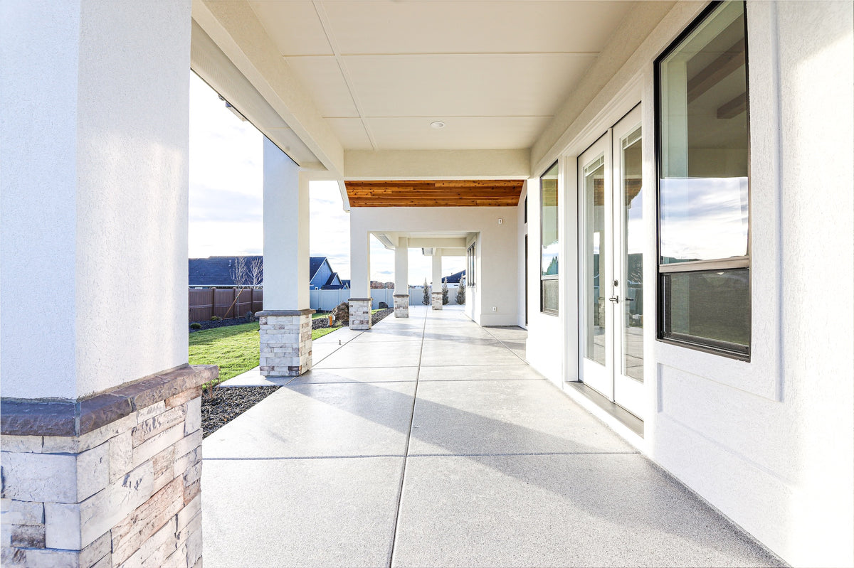 Modern outdoor patio area with white walls, glass doors, and a clear sky.