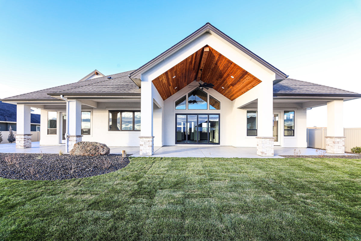 Modern house with a large covered porch and glass windows, set against a clear blue sky.