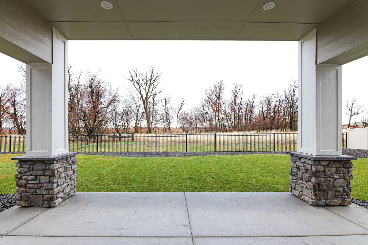 Covered outdoor patio with stone columns overlooking a grassy field and trees.