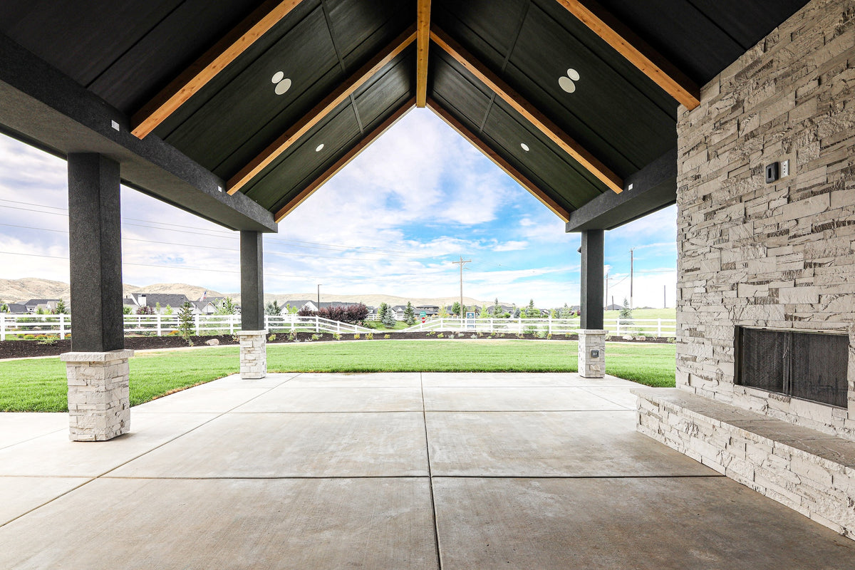 Covered outdoor area with stone walls and a vaulted ceiling, overlooking a grassy field.