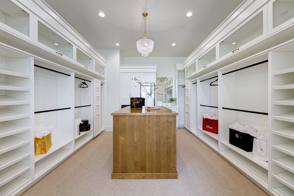 Modern walk-in closet with white shelves, wooden island, and various clothing items.