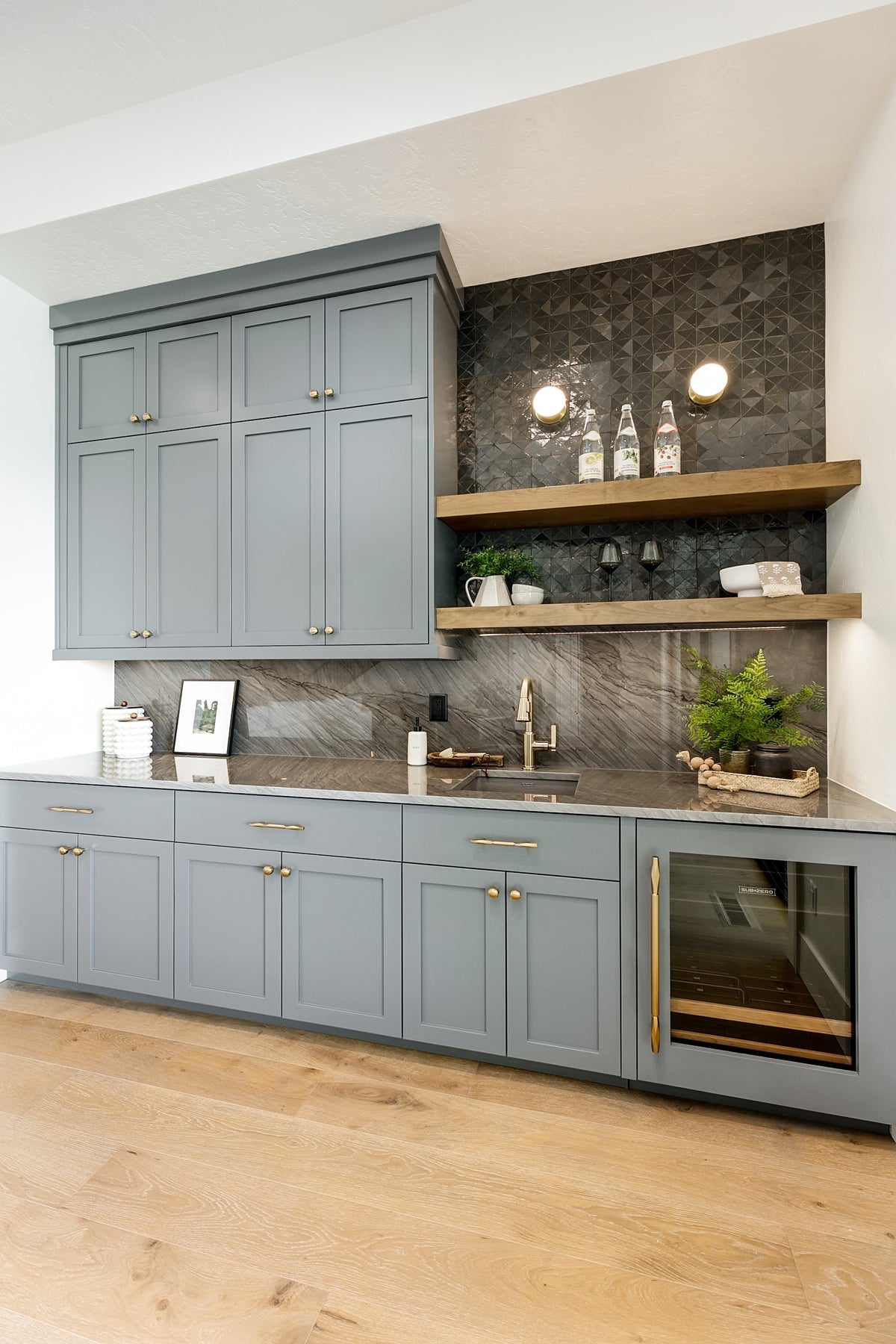 Modern kitchen with gray cabinets, wooden shelves, and marble countertop.