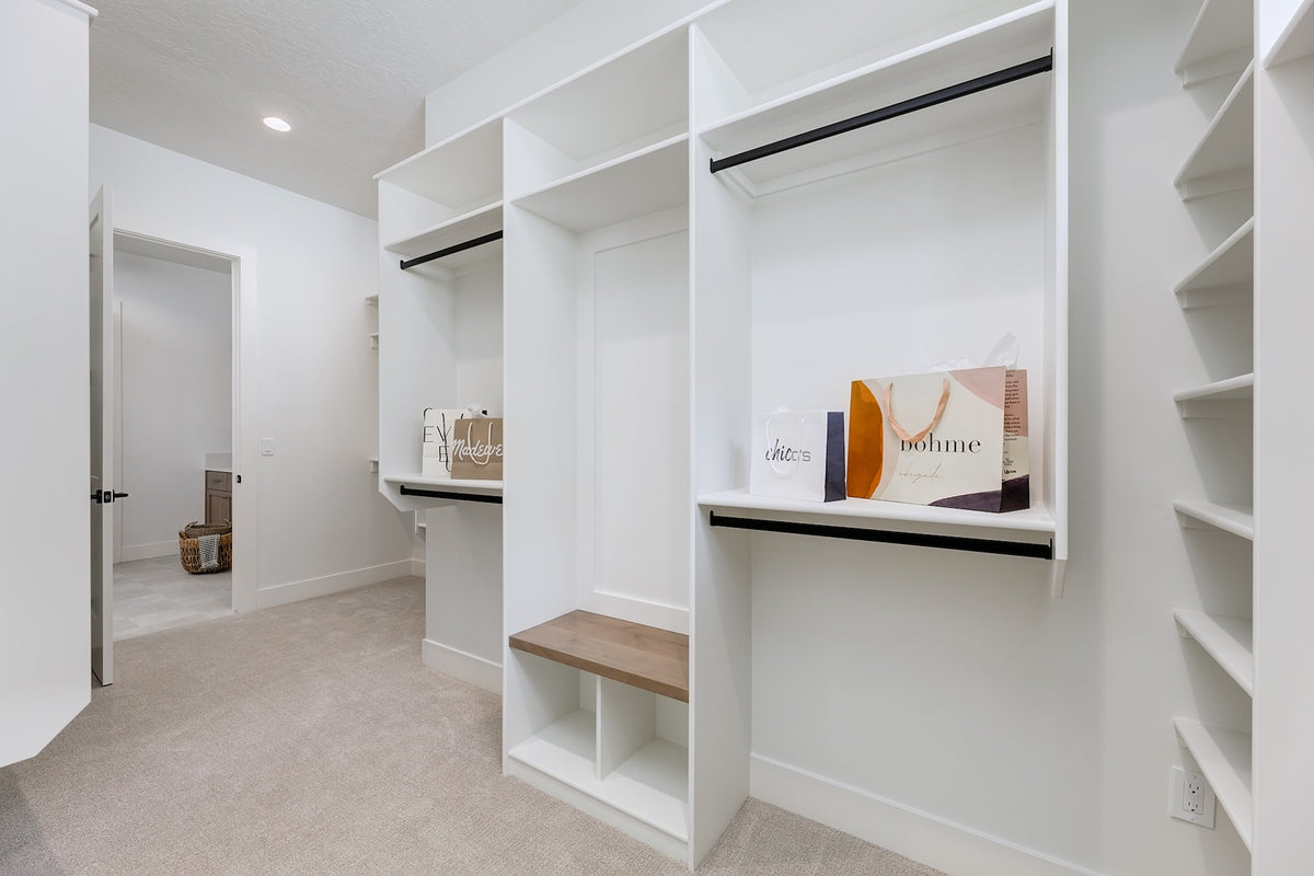 Modern walk-in closet with white shelves and a wooden bench.