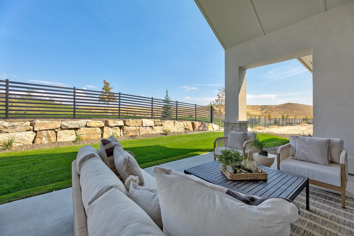 Outdoor patio with white furniture and a view of a garden and mountains.