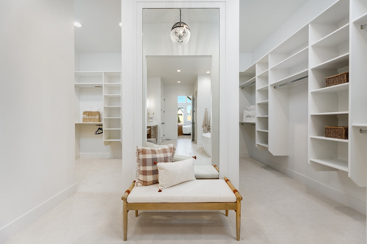 Modern walk-in closet with white shelves, a bench with cushions, and a mirror.