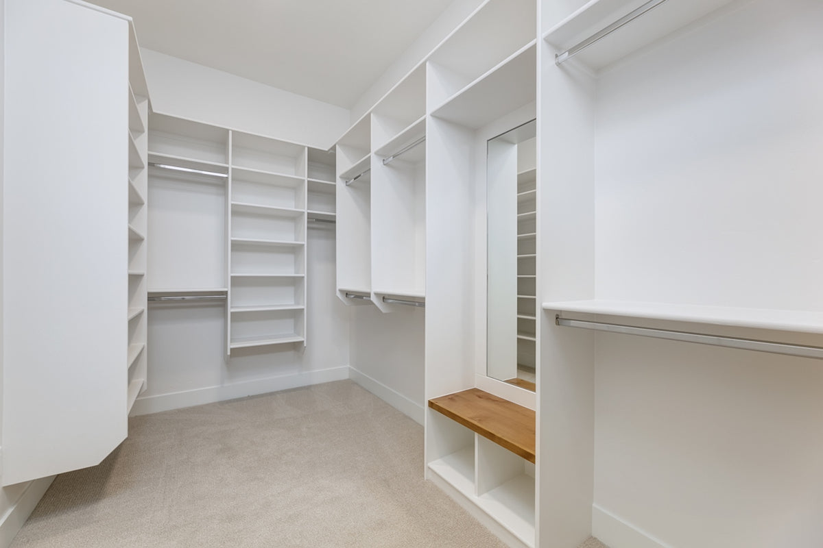 Empty white walk-in closet with shelves and a wooden bench.