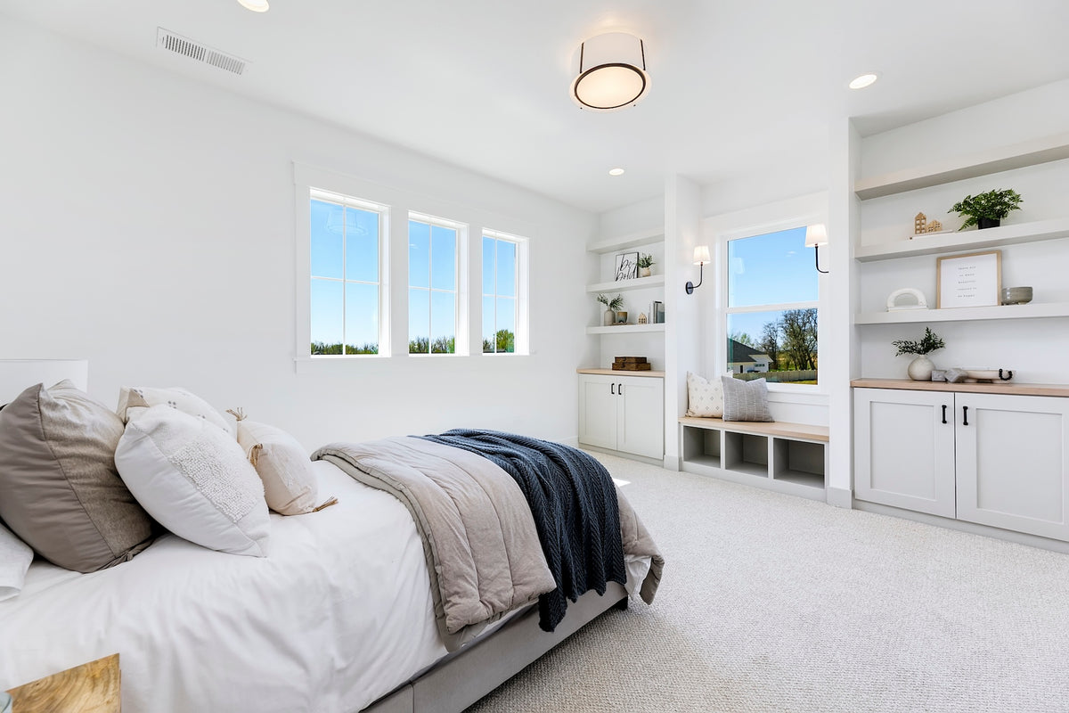 Modern bedroom with white walls, bed, and large windows overlooking a garden.