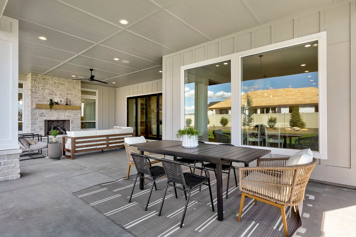 Modern outdoor patio with dining table and chairs, large windows, and fireplace.