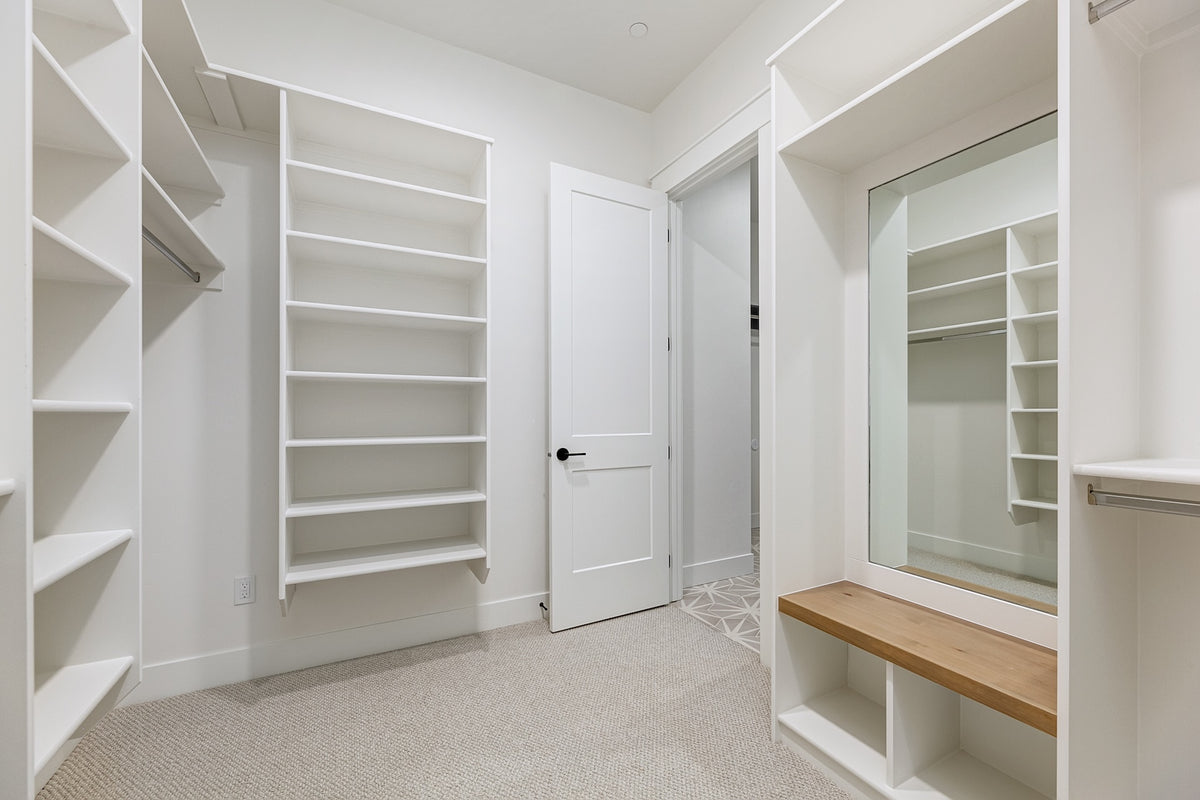 Closet with white shelves, a wooden bench, and a mirror.