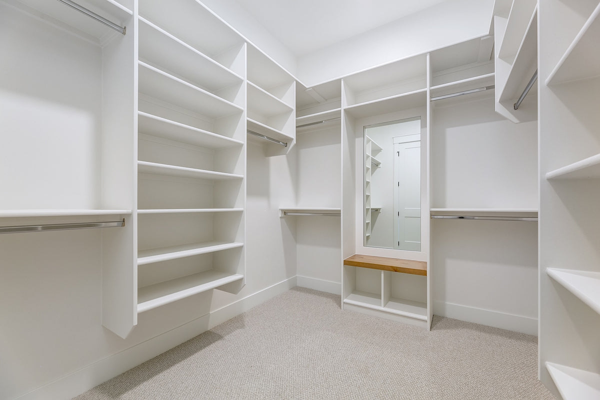 Empty white walk-in closet with shelves and a mirror.