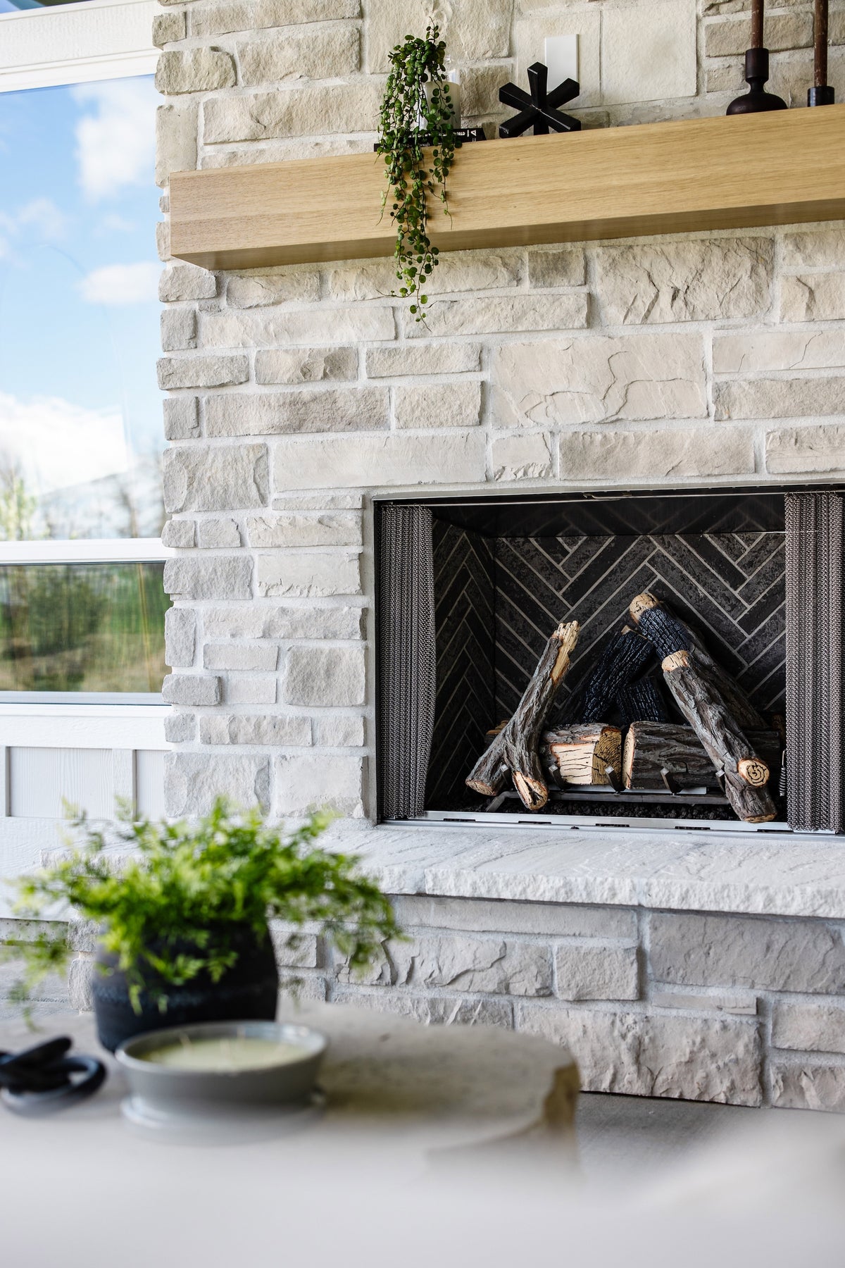 Outdoor fireplace with stone surround and wooden mantel, surrounded by greenery.