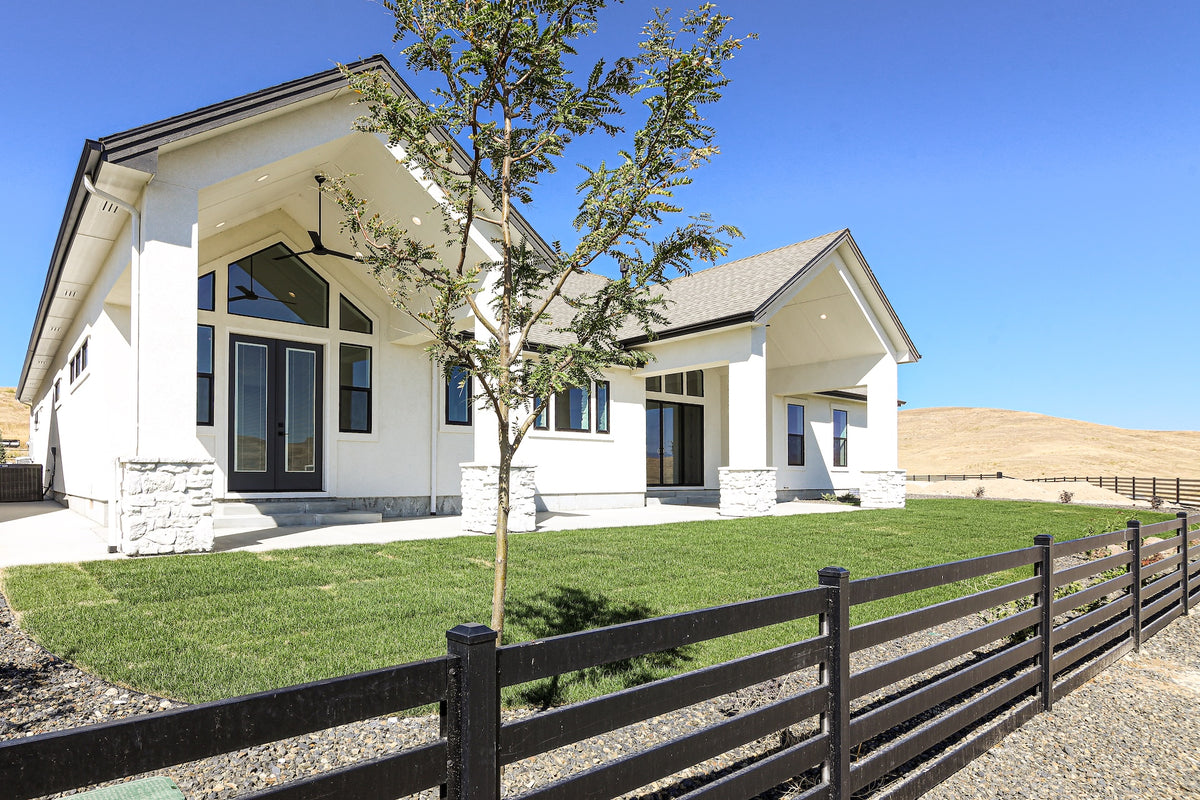 Modern house with white exterior and large windows, surrounded by green grass and a wooden fence.