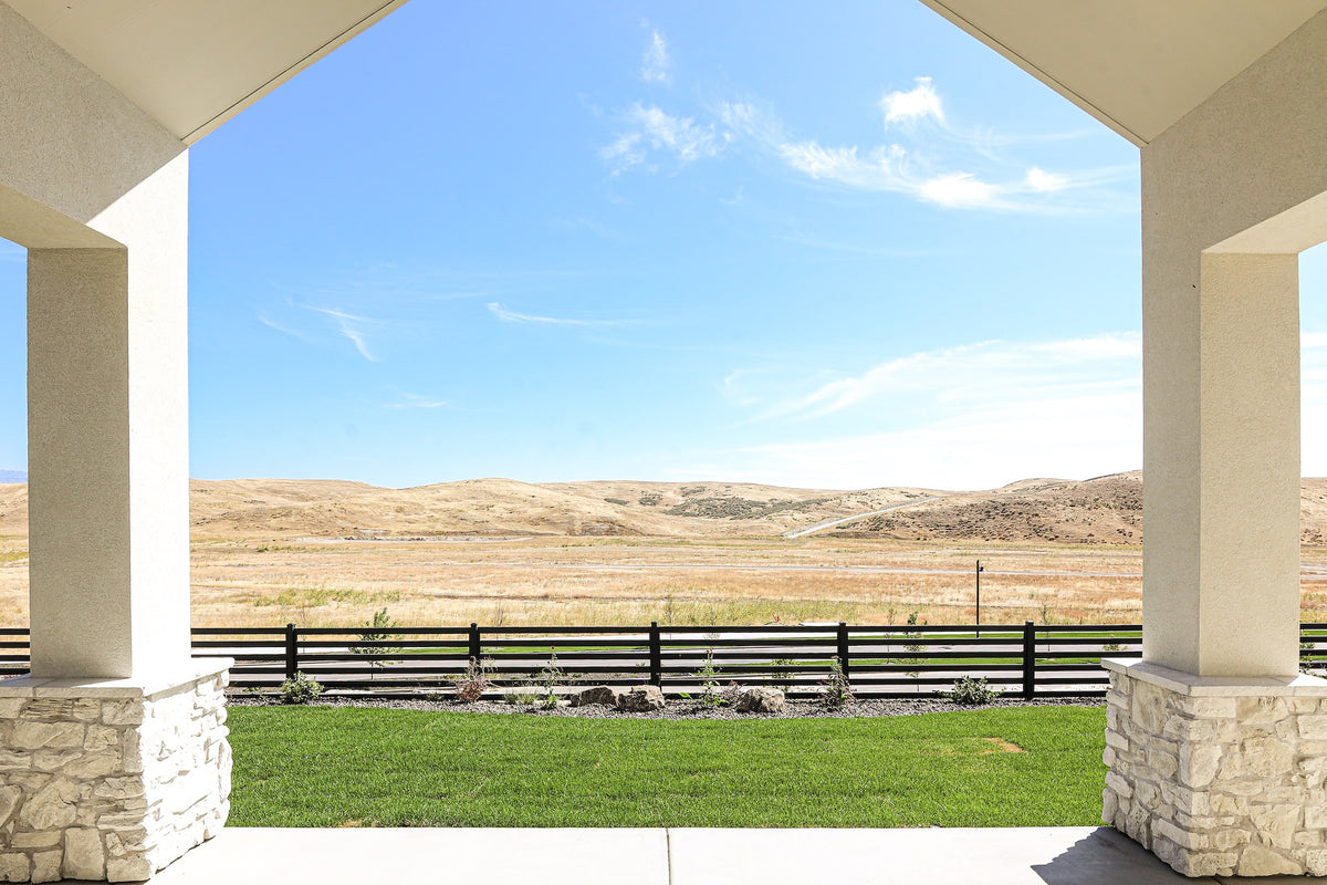 Covered patio with stone columns overlooking a scenic landscape with hills and a fence.