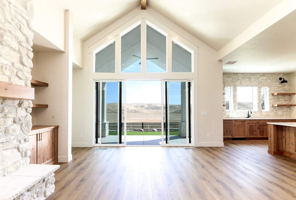 Modern living room with large windows, stone fireplace, and wooden floor.