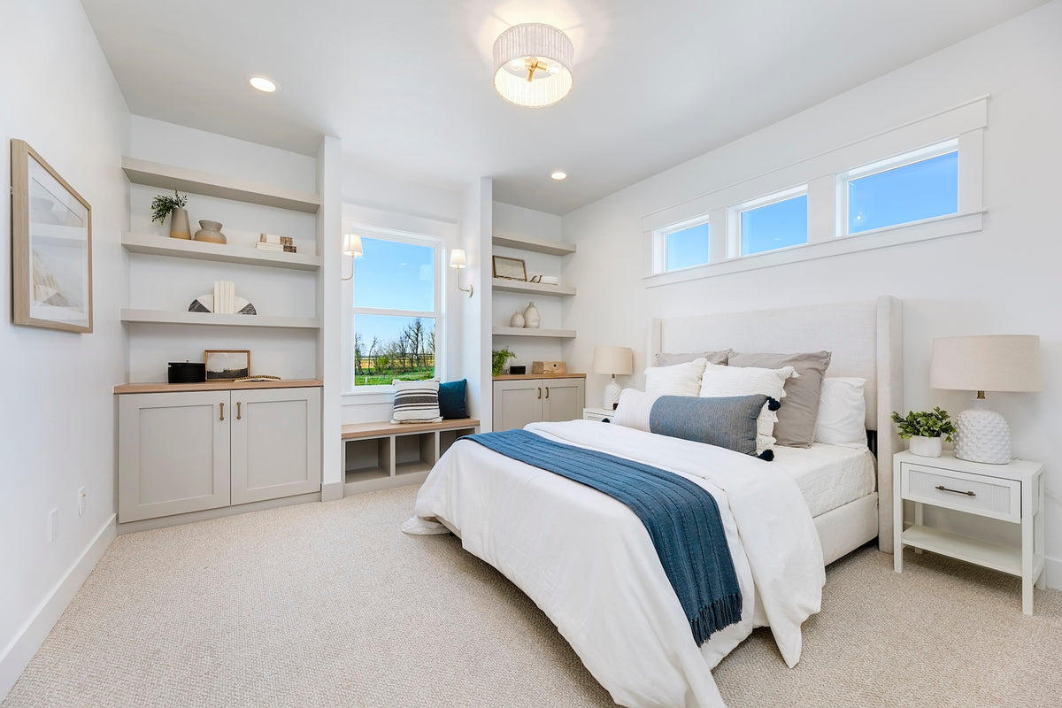 Modern bedroom with white bed, blue accent pillows, and a view of the ocean through large windows.