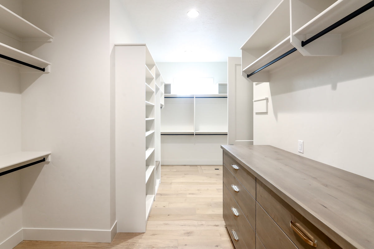 Modern walk-in closet with white shelves and wooden drawers.